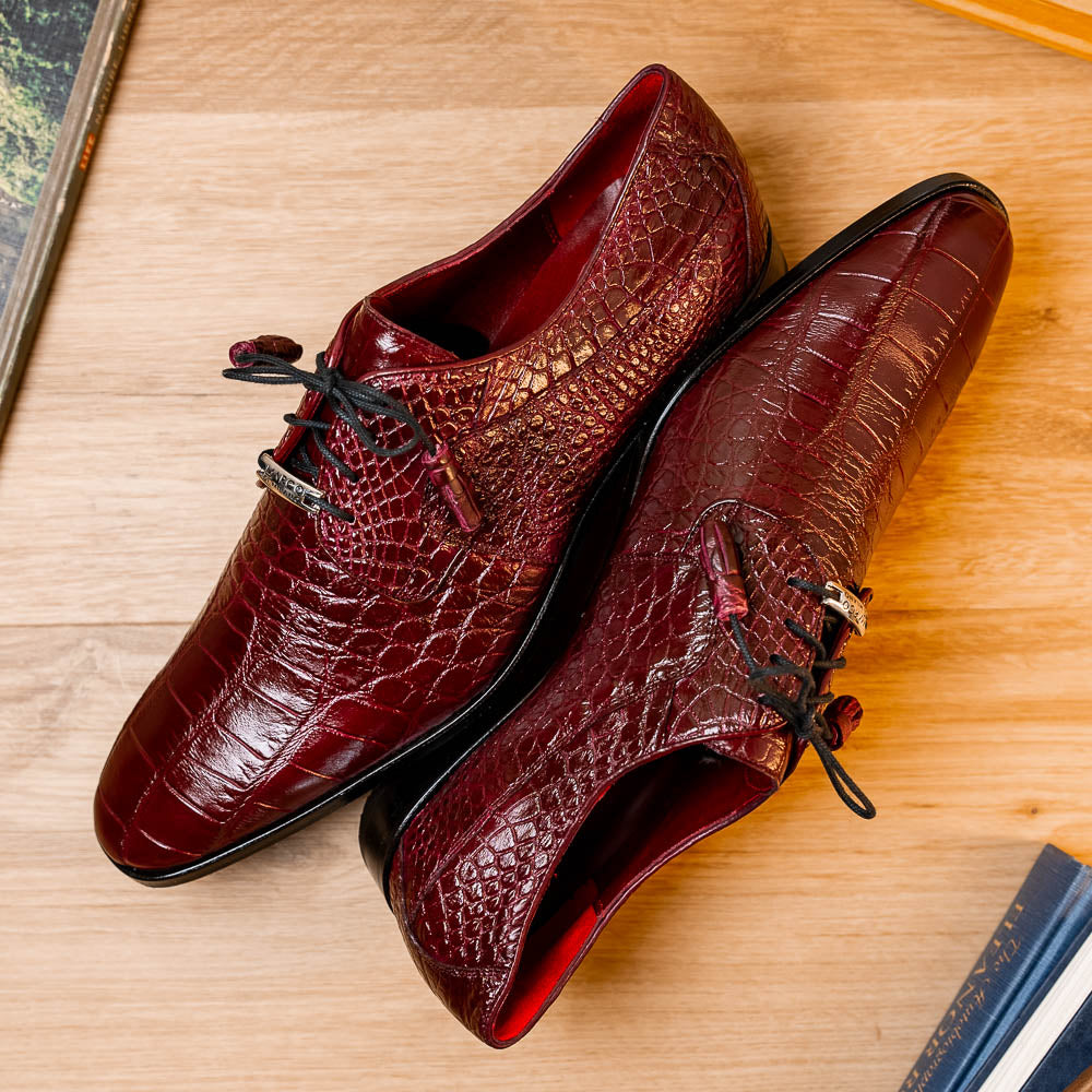 The Fitipaldi Wine by Marco Di Milano is a burgundy crocodile-pattern leather dress shoe with black laces, shown on its side to reveal the tan sole and logo—highlighting hand-painted details and luxury craftsmanship.