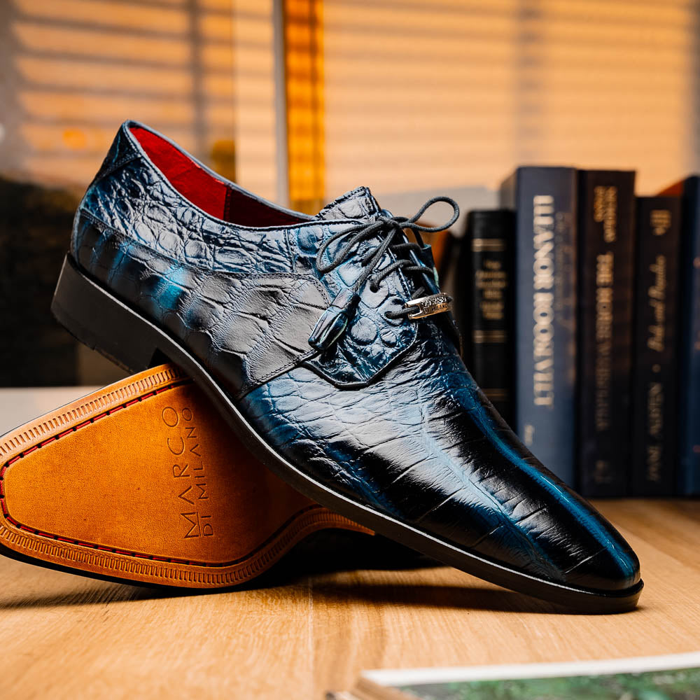 Fitipaldi Rustic Navy by Marco Di Milano: a pair of blue leather men’s dress shoes with a crocodile pattern, black soles, and lace-up fronts; one luxury shoe is shown on its side to display the tan sole.