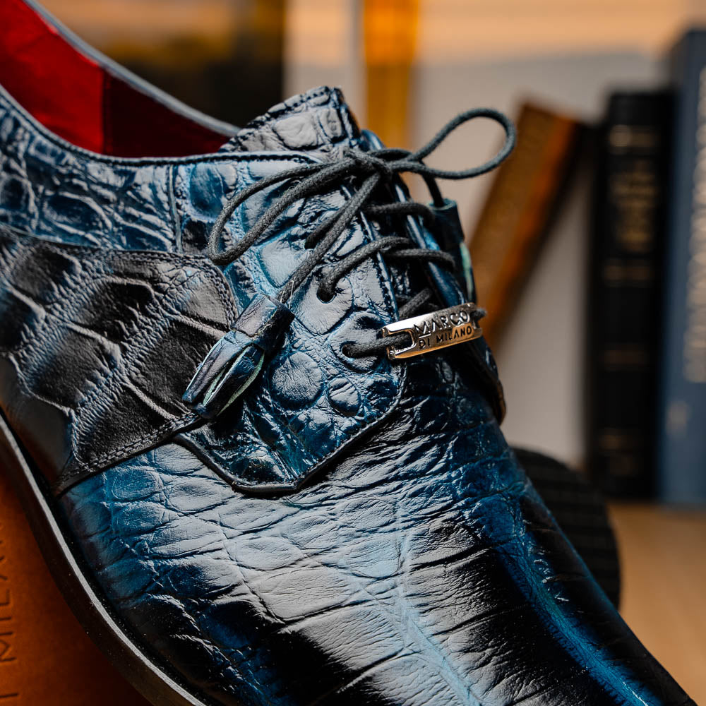 Fitipaldi Rustic Navy by Marco Di Milano: a pair of blue leather men’s dress shoes with a crocodile pattern, black soles, and lace-up fronts; one luxury shoe is shown on its side to display the tan sole.