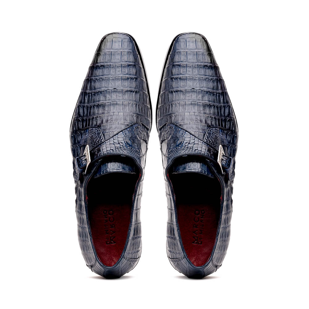 The Marco Di Milano Rovigo B Navy is a luxury men's monk strap shoe in blue crocodile-pattern leather, with one shoe upright and the other showing a tan sole stamped with the brand logo—perfect for dress shoe aficionados.