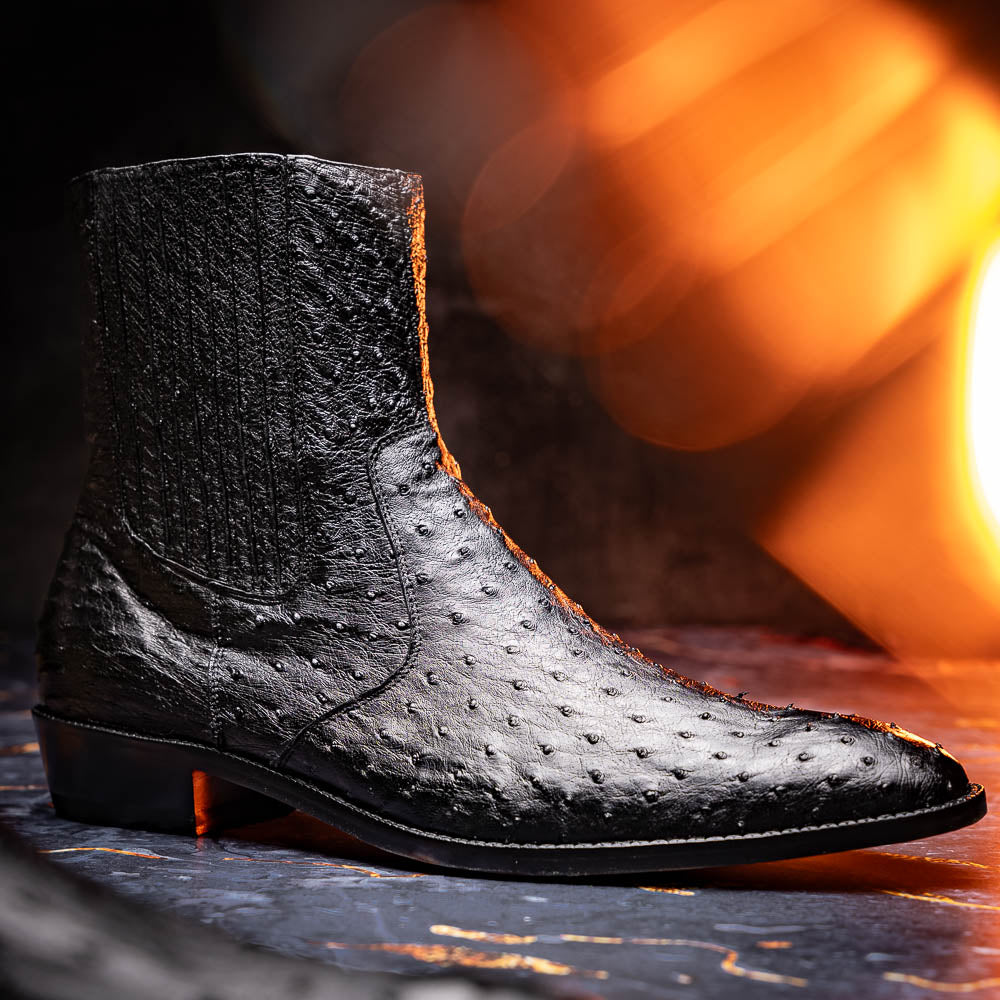 The Marco Di Milano Giorgio Black is a pair of luxury dress boots in genuine ostrich quill leather, showcasing a black ankle design, side zippers, brown leather soles, and visible sole branding—one boot upright, one on its side.