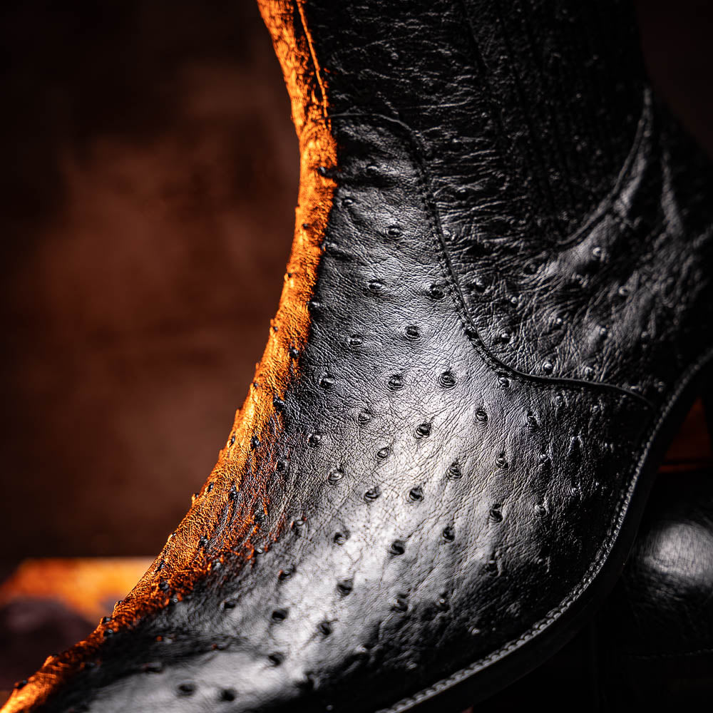 The Marco Di Milano Giorgio Black is a pair of luxury dress boots in genuine ostrich quill leather, showcasing a black ankle design, side zippers, brown leather soles, and visible sole branding—one boot upright, one on its side.