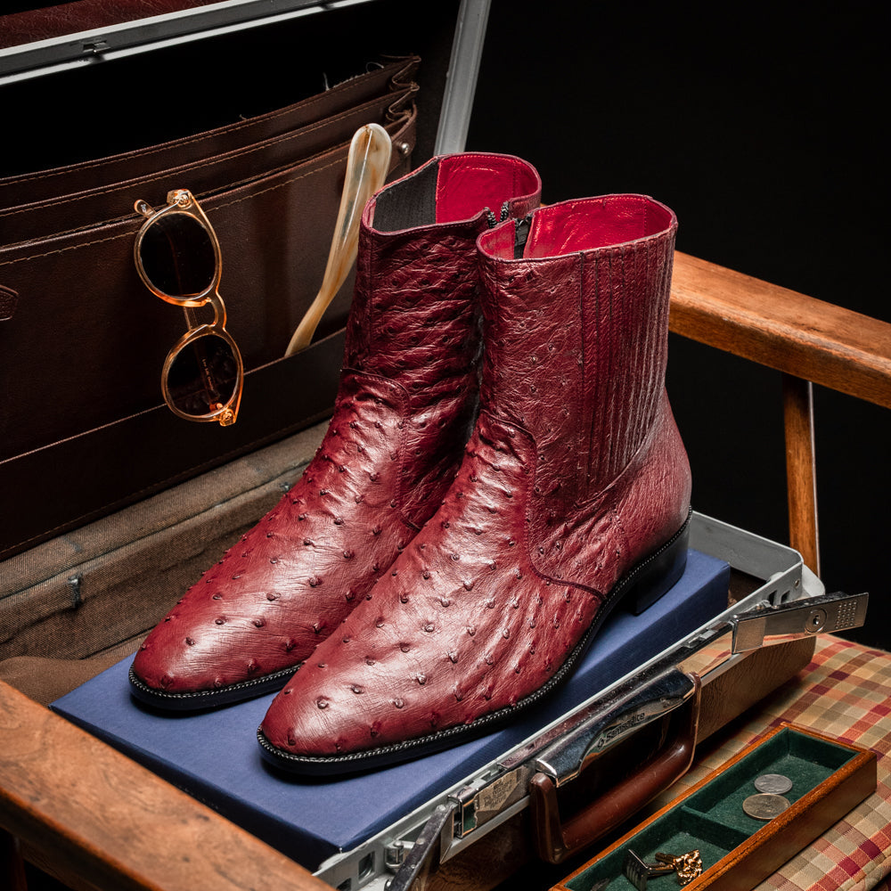 Introducing Giorgio Wine by Marco Di Milano: a pair of luxurious men's boots handcrafted in genuine burgundy ostrich leather, featuring a distinctive textured pattern, side zipper, elastic panel, and a sleek black sole—sophisticatedly presented against a white background.