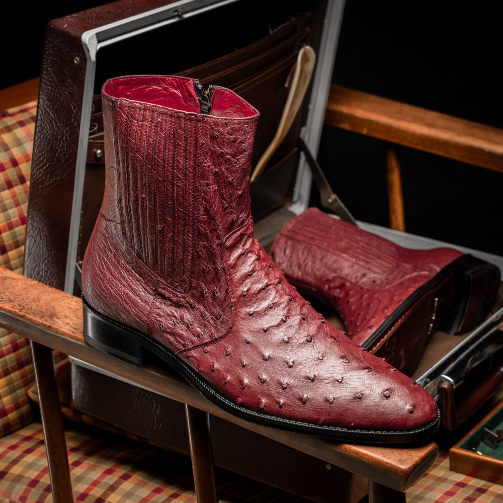 Introducing Giorgio Wine by Marco Di Milano: a pair of luxurious men's boots handcrafted in genuine burgundy ostrich leather, featuring a distinctive textured pattern, side zipper, elastic panel, and a sleek black sole—sophisticatedly presented against a white background.