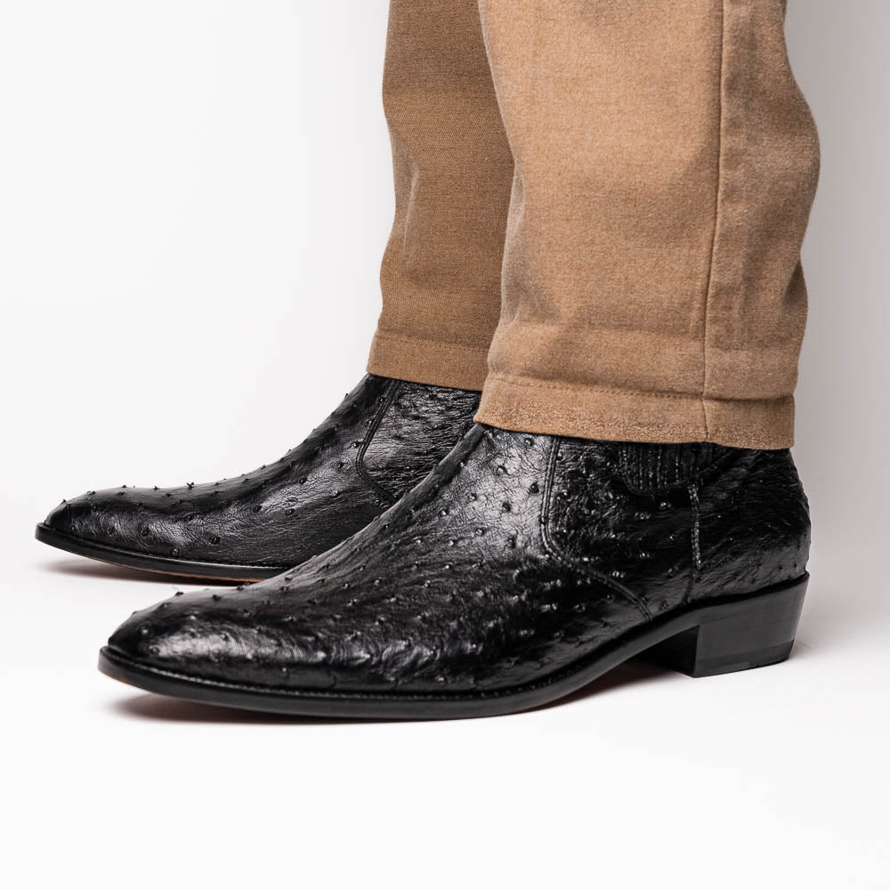 The Marco Di Milano Giorgio Black is a pair of luxury dress boots in genuine ostrich quill leather, showcasing a black ankle design, side zippers, brown leather soles, and visible sole branding—one boot upright, one on its side.