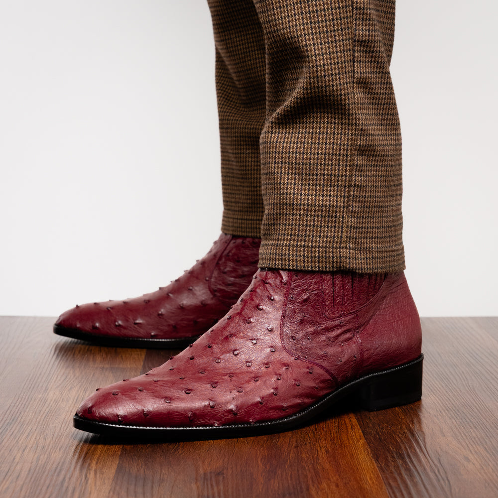 Introducing Giorgio Wine by Marco Di Milano: a pair of luxurious men's boots handcrafted in genuine burgundy ostrich leather, featuring a distinctive textured pattern, side zipper, elastic panel, and a sleek black sole—sophisticatedly presented against a white background.