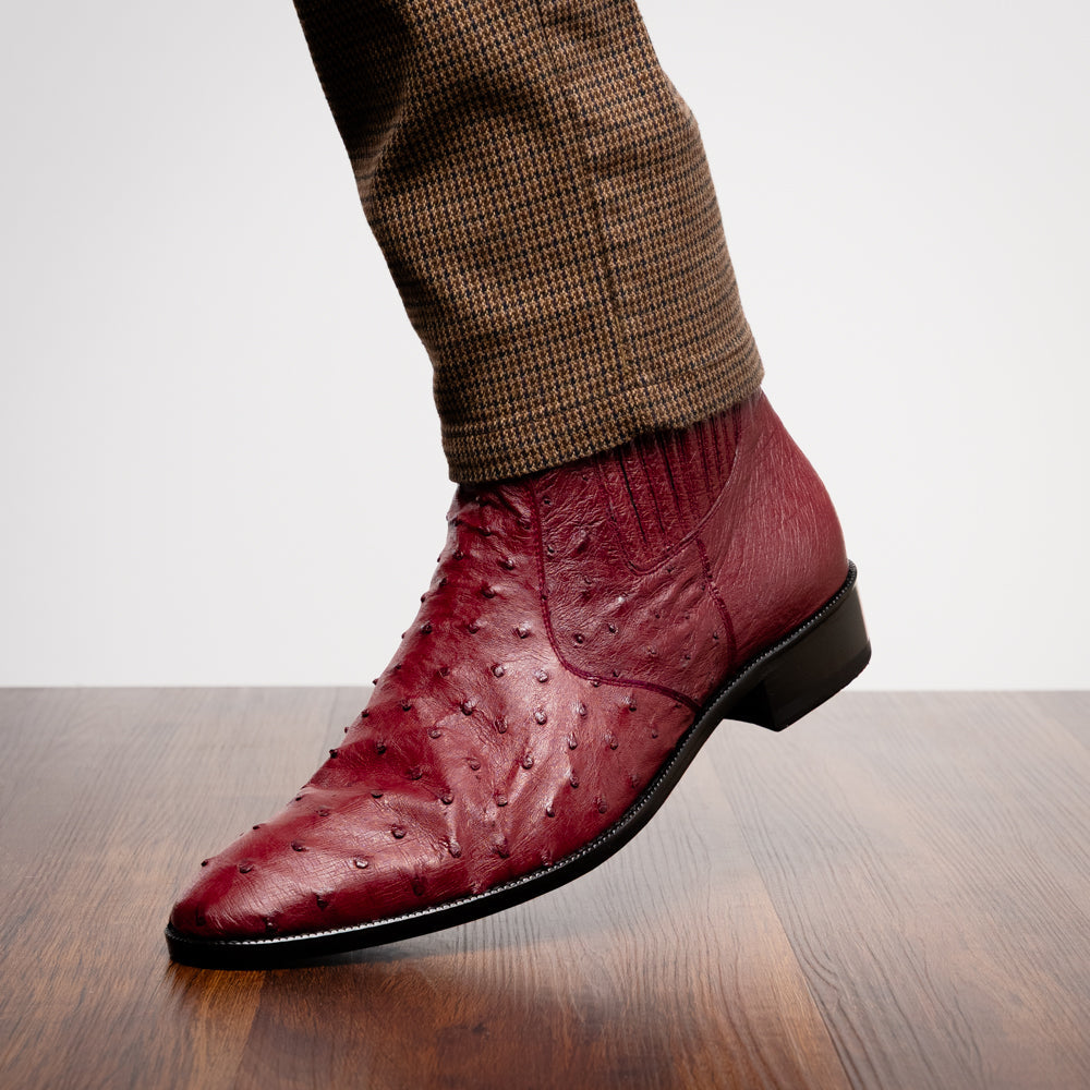 Introducing Giorgio Wine by Marco Di Milano: a pair of luxurious men's boots handcrafted in genuine burgundy ostrich leather, featuring a distinctive textured pattern, side zipper, elastic panel, and a sleek black sole—sophisticatedly presented against a white background.