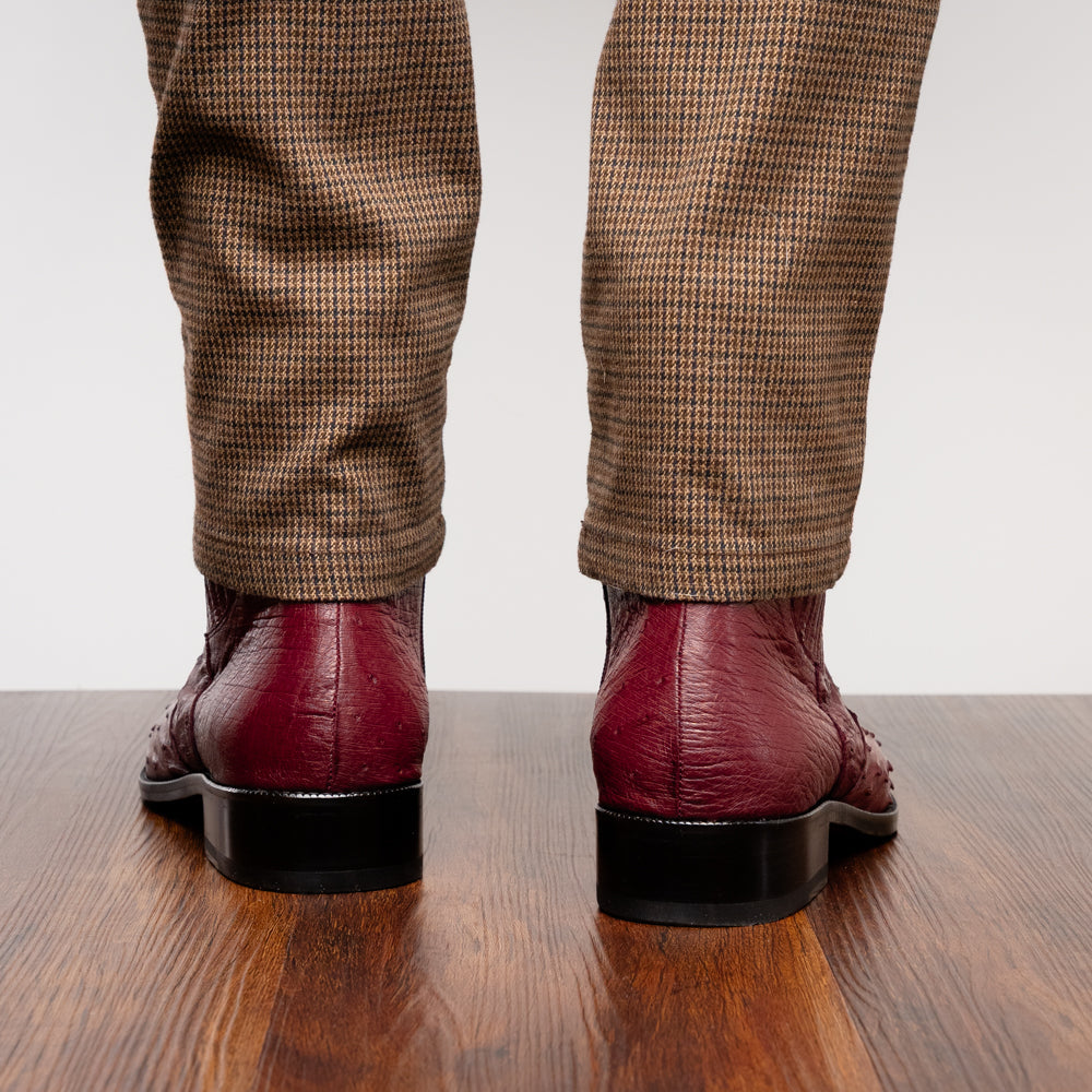 Introducing Giorgio Wine by Marco Di Milano: a pair of luxurious men's boots handcrafted in genuine burgundy ostrich leather, featuring a distinctive textured pattern, side zipper, elastic panel, and a sleek black sole—sophisticatedly presented against a white background.