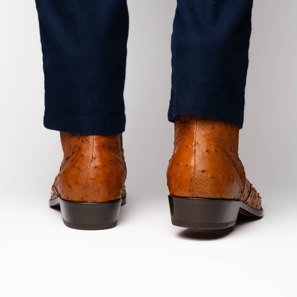 The Giorgio Brandy dress boots by Marco Di Milano feature genuine brown ostrich quill leather, hand-painted finishes, a side zipper, and a textured design—one upright and one lying down to showcase the sole's craftsmanship.