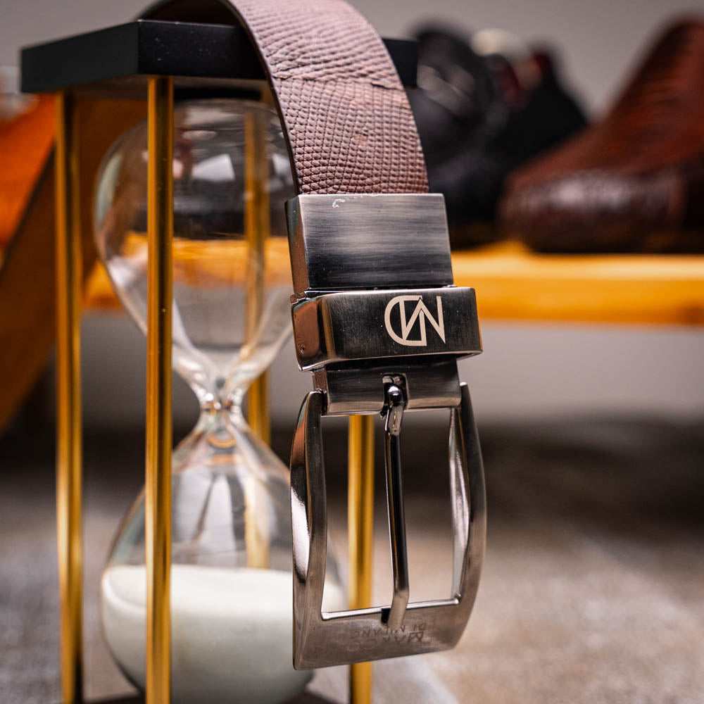 The Giovanni Belt Brown by Marco Di Milano is a dark brown leather belt with a textured pattern, finished with a silver buckle engraved with "Marco" and the "MD" logo, crafted from genuine lizard ring-caiman belly leather.