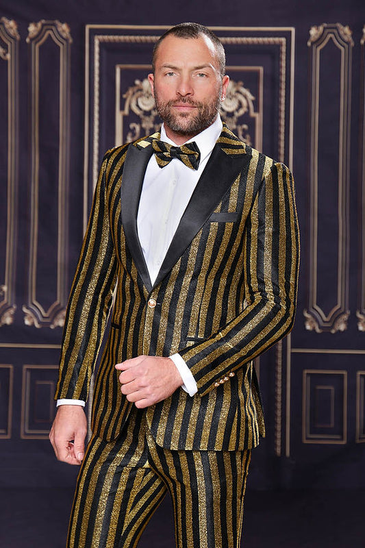 A man confidently poses in a Manzini HEATHER Men's Slim-Fit 2-Piece Glitter Stripe Stage Prom Suit in gold, complete with a matching bow tie, standing before a dark decorative background.