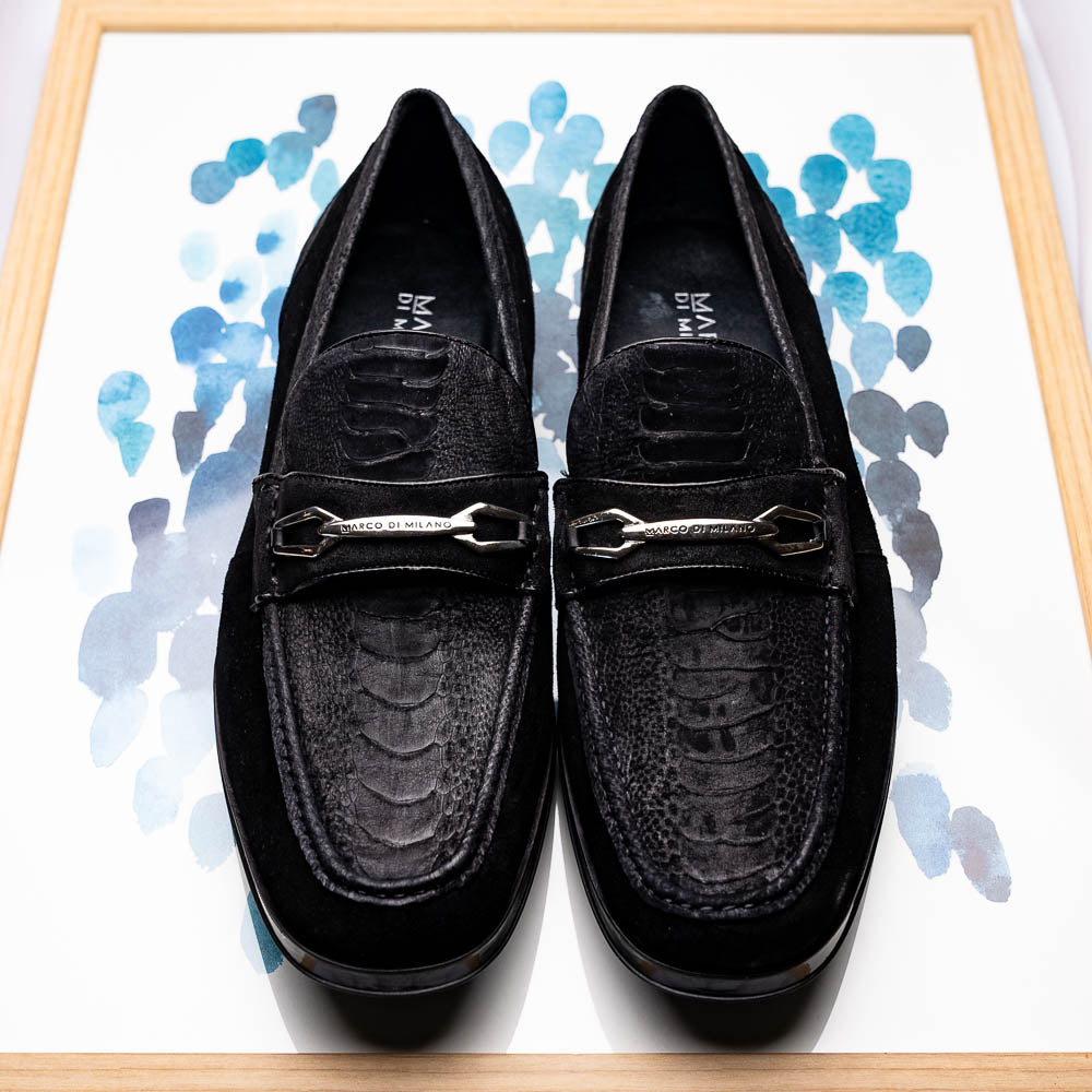 A pair of Marco Di Milano Hugo Black sueded ostrich leg loafers with metal chain detailing and textured rubber soles, one upright and one on its side, display refined luxury craftsmanship.