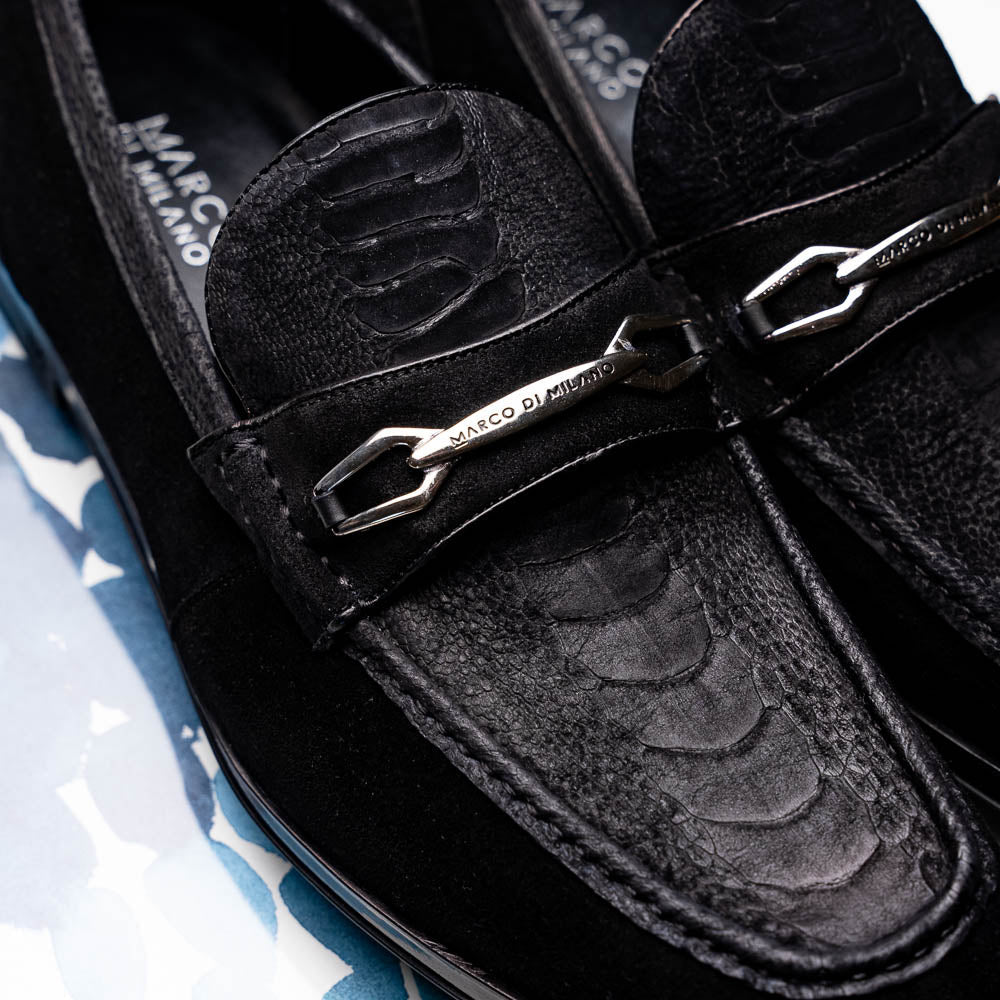 A pair of Marco Di Milano Hugo Black sueded ostrich leg loafers with metal chain detailing and textured rubber soles, one upright and one on its side, display refined luxury craftsmanship.