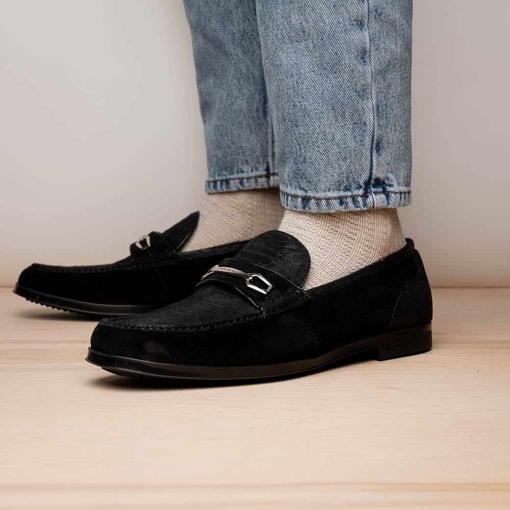 A pair of Marco Di Milano Hugo Black sueded ostrich leg loafers with metal chain detailing and textured rubber soles, one upright and one on its side, display refined luxury craftsmanship.