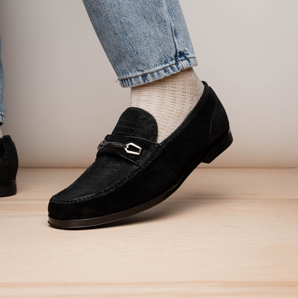 A pair of Marco Di Milano Hugo Black sueded ostrich leg loafers with metal chain detailing and textured rubber soles, one upright and one on its side, display refined luxury craftsmanship.