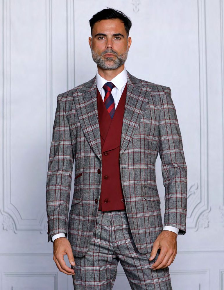 A bearded man wearing the Insomnia INSOMNIA PARIS-1 3PC tailored fit burgundy suit, featuring a gray plaid pattern and red waistcoat, stands against a white textured wall.
