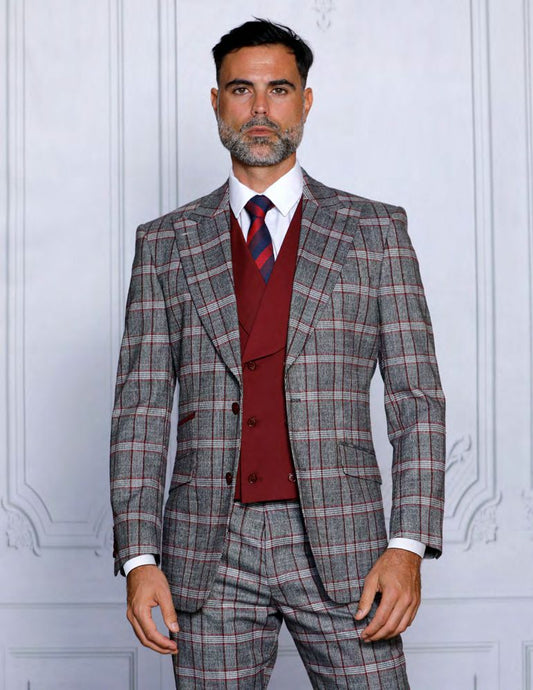 A bearded man wearing the Insomnia INSOMNIA PARIS-1 3PC tailored fit burgundy suit, featuring a gray plaid pattern and red waistcoat, stands against a white textured wall.