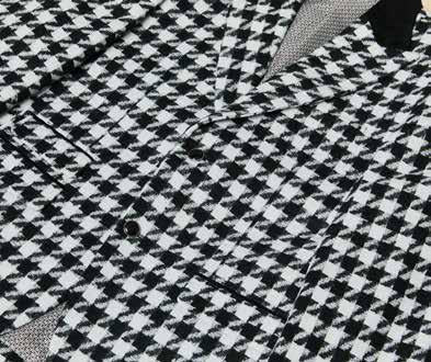 The Inserch Wool Blend Houndstooth Check Peak Lapel Suit in Black/White, from the brand Inserch, creates a sophisticated ensemble with its subtle modern suede trim. Paired with a sleek black shirt, the individual stands confidently with one hand in their pocket against a plain background.