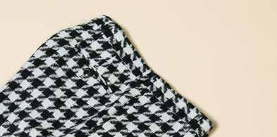 The Inserch Wool Blend Houndstooth Check Peak Lapel Suit in Black/White, from the brand Inserch, creates a sophisticated ensemble with its subtle modern suede trim. Paired with a sleek black shirt, the individual stands confidently with one hand in their pocket against a plain background.