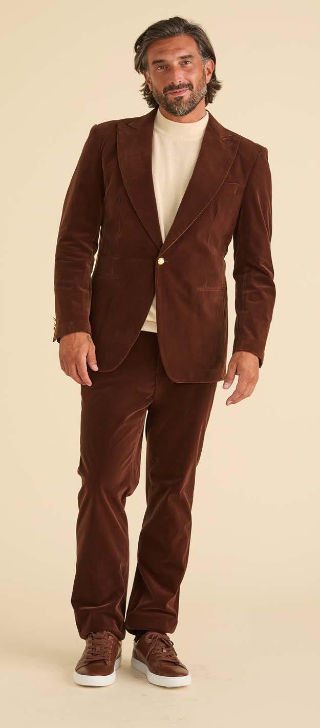 A man stands facing forward, wearing the Inserch Velvet Blazer BL007-131 Swiss Chocolate by Inserch with a cream turtleneck and brown sneakers, against a neutral background.