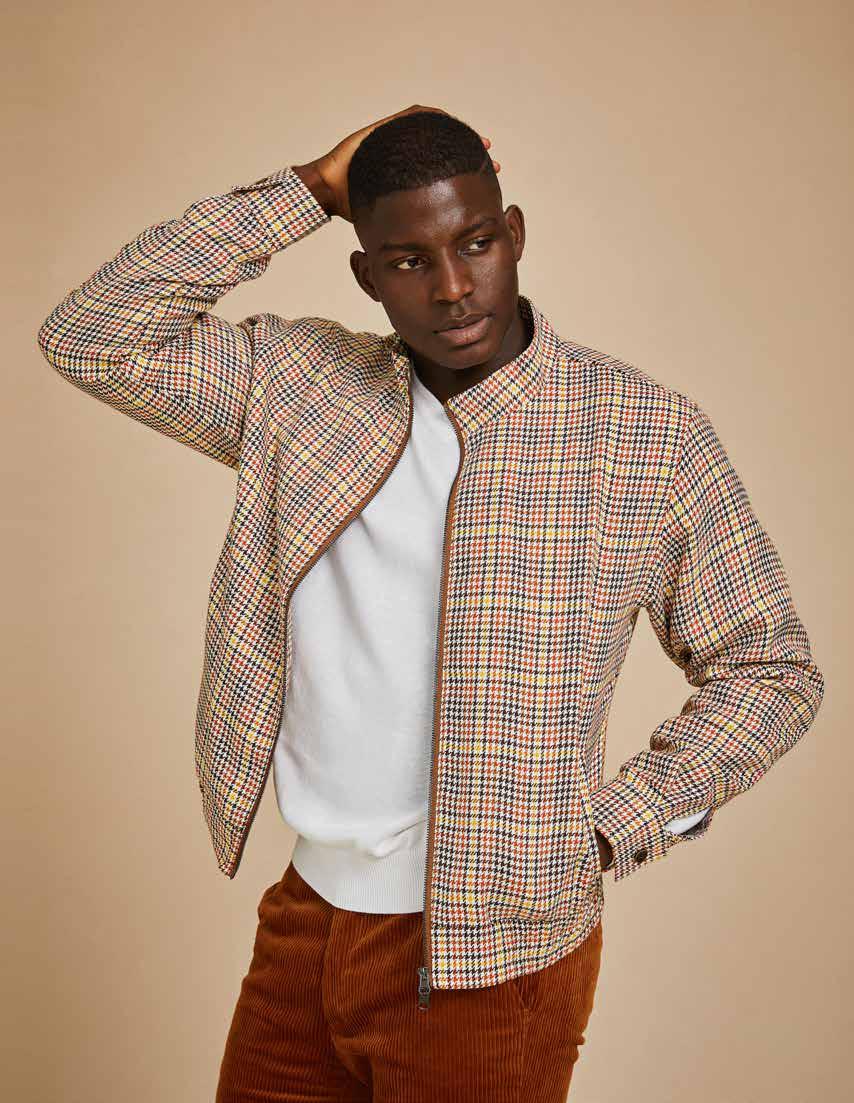 A man wearing the Inserch Micro Check Full Zip Jacket JS265-64 Mocha, featuring a unique print lining, pairs it with a yellow turtleneck, blue jeans, and brown sneakers as he stands against a beige background.