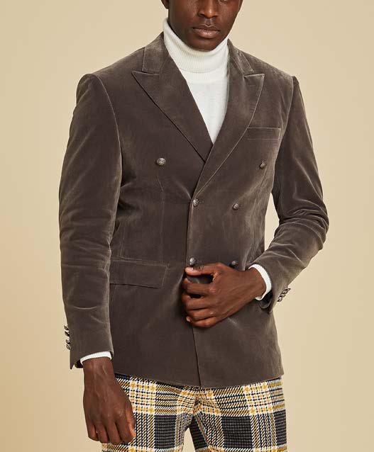 A man wears the Inserch DB Velvet Blazer BL502-33 Grey by Inserch, styled with a white turtleneck and plaid yellow, black, and white pants against a beige background.