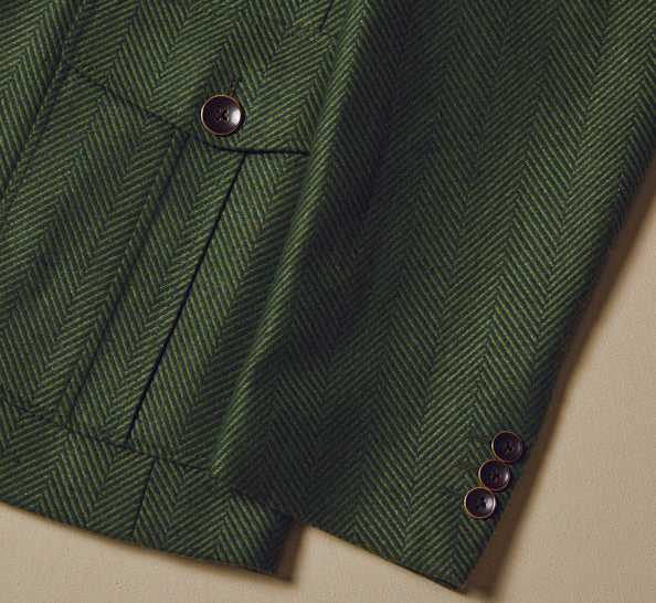 Dressed in an Inserch 4 Pocket Wool Blend Herringbone Blazer BL263-19 Olive, paired with a light turtleneck, an individual stands against a neutral backdrop, radiating contemporary sophistication.