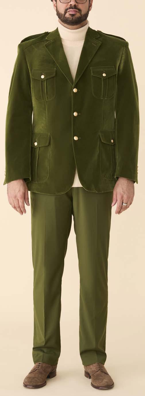 A man stands against a beige background wearing the Inserch Velvet Military Blazer BL569-19 Olive by Inserch, styled with gold military shank buttons, a cream turtleneck sweater, and brown shoes.