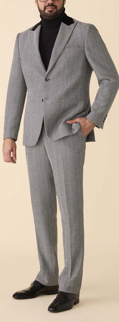 A person showcases modern style against a beige background, wearing the Inserch Herringbone Suit BL273-00041 Black/White by Inserch, paired with a black turtleneck and black dress shoes.