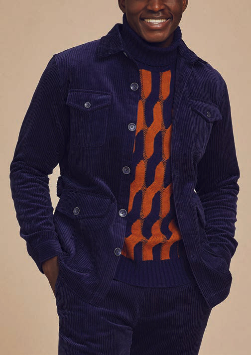 Wearing the Inserch 4-Pocket Cord Suit BL267-11 in a modern fit, complemented by an orange and blue patterned sweater, a man stands confidently against a beige background. The navy blue corduroy jacket and pants from Inserch add texture to his ensemble, highlighted by an adjustable back tab for tailored comfort.