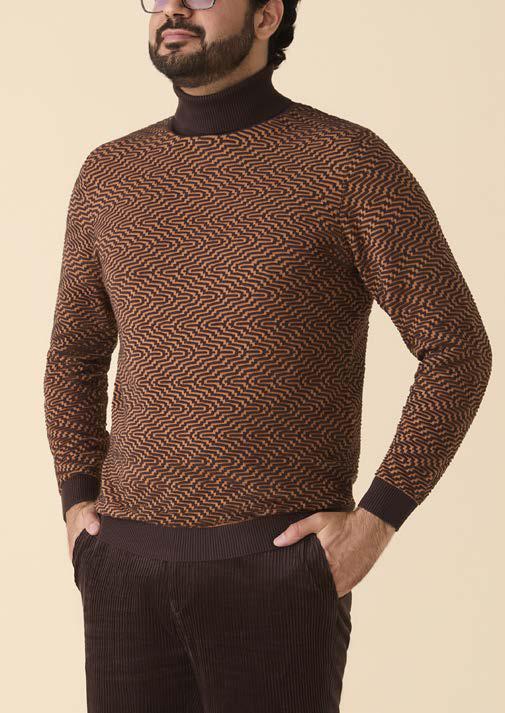 A person wearing the Inserch Intarsia Turtleneck Sweater SW304-00043 Espresso by Inserch, featuring a brown and orange geometric pattern with dark brown accents, paired with dark brown pants, stands against a beige background.