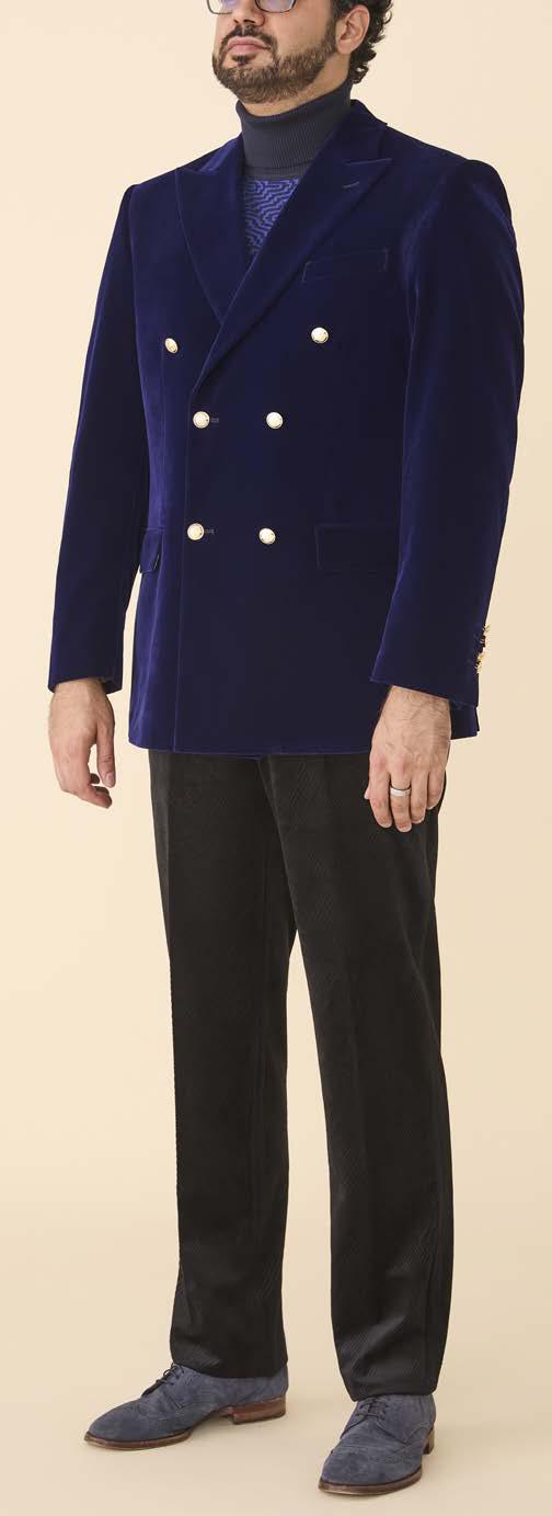 A man wears the Inserch DB Velvet Blazer BL502-13 Royal Blue by Inserch, styled with black trousers, a dark turtleneck, and blue shoes, set against a plain beige background.