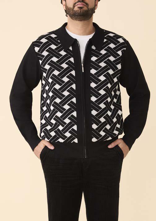 A man stands with hands in pockets against a beige background, wearing the Inserch Geometric Full Zip Sweater SW908-00001 Black by Inserch, featuring a regular fit and bold black-and-white geometric intarsia pattern on the front.