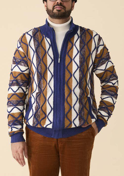 Man wearing the Inserch Bouclé Yarn Graphic Full Zip Sweater SW614-00001 Royal Blue, styled with a white turtleneck and brown corduroy pants against a beige background.