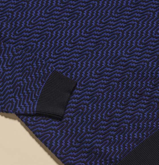 A man wearing the Inserch Intarsia Turtleneck Sweater SW304-00036 Ink by Inserch and navy pants stands against a beige background with one hand in his pocket.