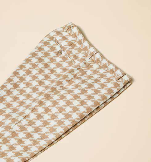 A person wearing Inserch Houndstooth Pants (P264-09 Khaki) in a modern fit, with a brown and white wool-blend houndstooth pattern, has their hands in pockets while paired with white sneakers and stands against a beige background.