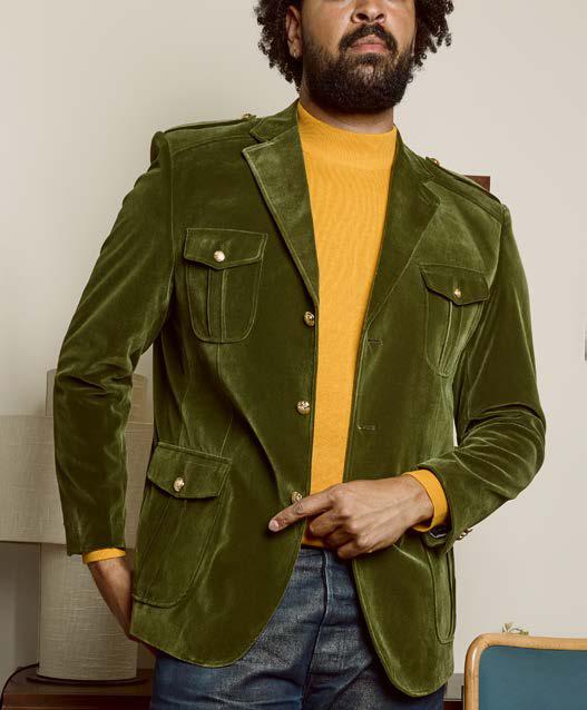An individual is seen indoors wearing the Inserch Velvet Military Blazer BL569-00019 Olive, distinguished by its military shank buttons, layered over a mustard yellow turtleneck and paired with blue jeans.