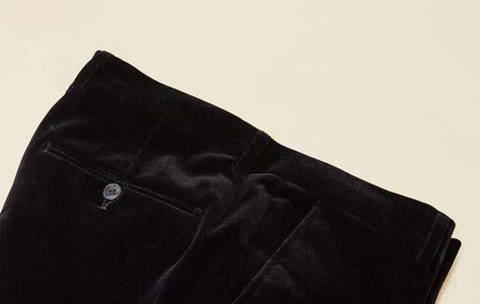 A folded pair of Inserch Velvet Pants P502-00001 in black is displayed on a beige background, showcasing a modern fit with a visible back pocket and button.