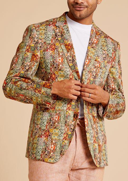 A man wearing the Inserch Patchwork Print Blazer BL261-35 Rust, featuring a colorful digital abstract design and modern fit, adjusts his cotton stretch jacket over a white shirt and pink pants.
