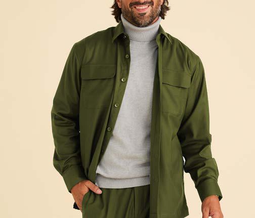 A man is wearing the Inserch Two-Pocket Shirt SE004-00020 in Chive—an olive green, regular fit, long sleeve shirt by Inserch—paired with matching pants over a light gray turtleneck sweater, standing and smiling against a beige background.