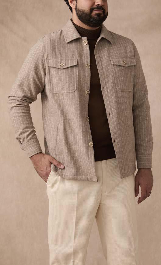 A man stands with one hand in his pocket against a plain background, wearing the Inserch Wool Blend Flannel Jacket JS280-00015 Stone—a regular-fit beige striped wool blend flannel jacket with marled buttons—over a brown shirt and cream pants.