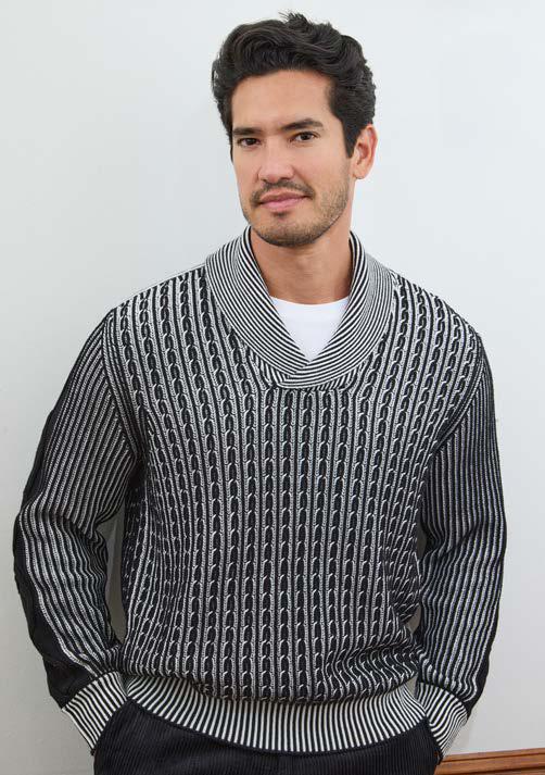 A man with short dark hair and facial hair stands against a plain white wall with his hands in his pockets, wearing the Inserch Shawl Collar Cable Sweater SW005-00001 Black by Inserch, crafted from a comfortable cotton-acrylic blend featuring a stylish yarn-dyed pattern.