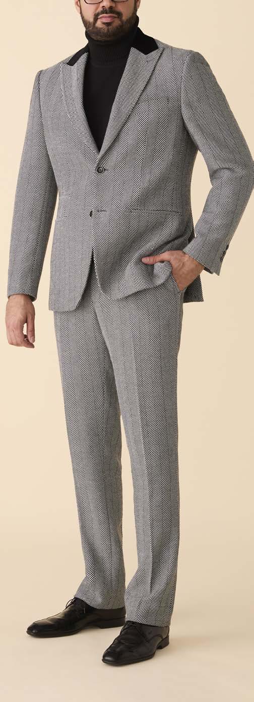 A person wearing the Inserch Herringbone Blazer BL273-00041 in Black/White by Inserch, paired with a black turtleneck and black dress shoes, stands with one hand in their pocket against a plain background.