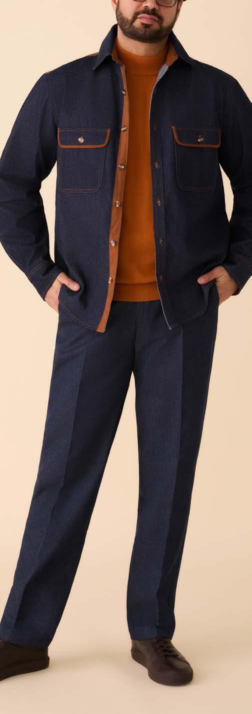 Someone stands against a beige background wearing the Inserch Denim Shirt w/ Suede Trim 2pc Set SE005-P005-00195 Indigo from Inserch, featuring a dark blue two-pocket jacket with brown suede trim and matching denim pants.