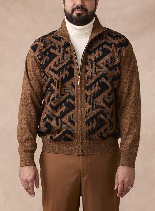 A man wearing the Inserch Full Zip Sweater SW616-00027 Aztec by Inserch—a brown intarsia sweater with a geometric black pattern—paired with a white turtleneck and brown pants, standing against a beige background.