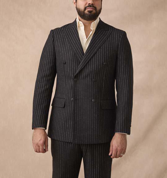 A man wearing the Inserch Wool Blend Flannel DB Stripe Suit SU660280L-00001 Black by Inserch along with a light-colored shirt, standing against a plain beige background.