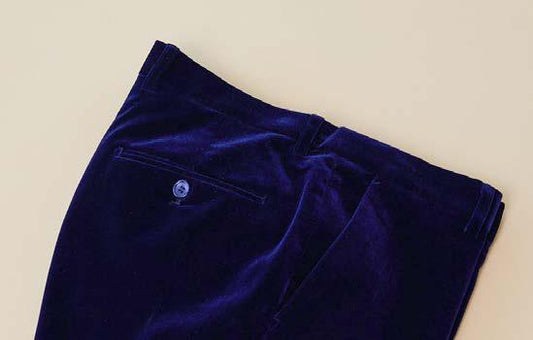 A pair of folded Inserch Velvet Pants P502-00013 in royal blue, featuring a modern fit with a flat front, back pocket, and button closure, is displayed on a light beige surface.