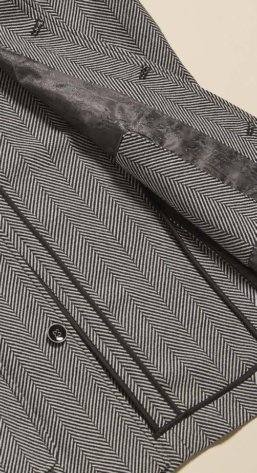 A person wearing the Inserch Herringbone 4 Pocket Jacket JS273-00041 Black/White by Inserch over a white turtleneck, black pants, and dark shoes stands against a plain beige background.