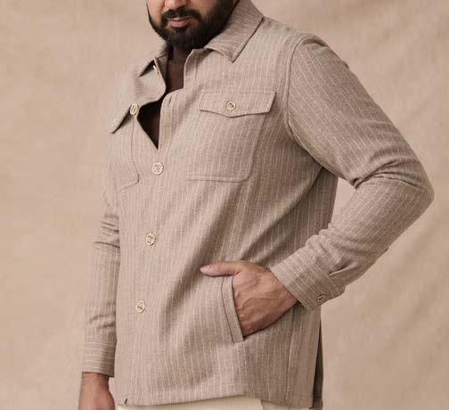 A man stands with one hand in his pocket against a plain background, wearing the Inserch Wool Blend Flannel Jacket JS280-00015 Stone—a regular-fit beige striped wool blend flannel jacket with marled buttons—over a brown shirt and cream pants.