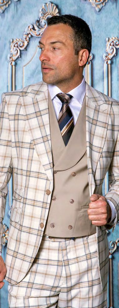 A man wears the INSOMNIA PARIS-5 3PC Compose Tailored Fit Beige Suit by Insomnia, featuring a tan double-breasted vest, white shirt, and striped tie, standing before an ornate blue and gold backdrop.